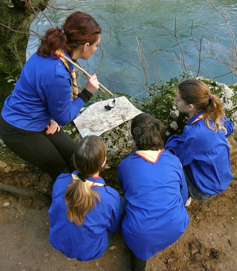 Four scouts (best friends) learn the nature of how to orient a map and compass. A grown woman with a cane on the map indicates the direction of movement. Vertical color photo. Four scouts (best friends) learn the nature of how to orient a map and compass. A grown woman with a cane on the map indicates the direction of movement. Vertical color photo.