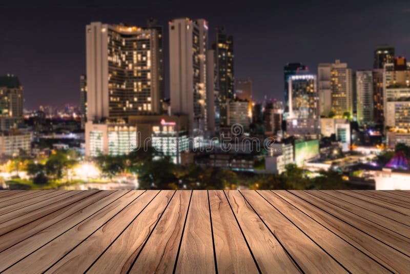 Scrittorio di legno superiore con il fondo urbano della sfuocatura di vista di notte della città, tavola di legno immagine stock Scrittorio di legno superiore con il fondo urbano della sfuocatura di vista di notte della città, tavola di legno immagine stock