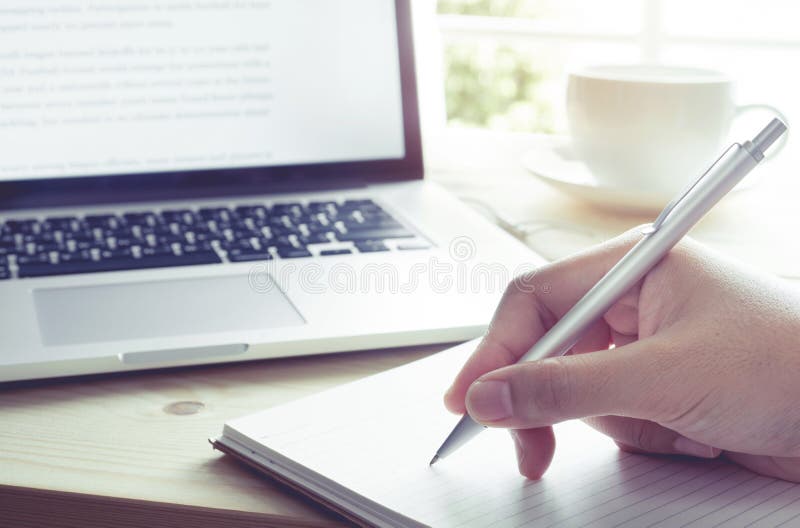 Scrittura della mano sul taccuino con il computer portatile Momento di ispirazione immagini stock libere da diritti