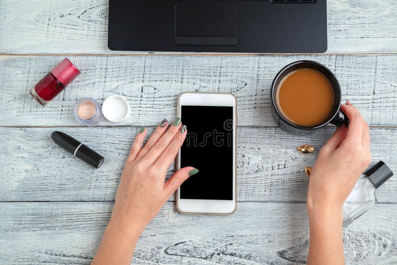 Scrivania posto di lavoro femminile mani, smartphone, laptop, Coppa del caffè, profumi e cosmetici da donna la vista dall'alto st fotografia stock Scrivania posto di lavoro femminile mani, smartphone, laptop, Coppa del caffè, profumi e cosmetici da donna la vista dall'alto st fotografia stock