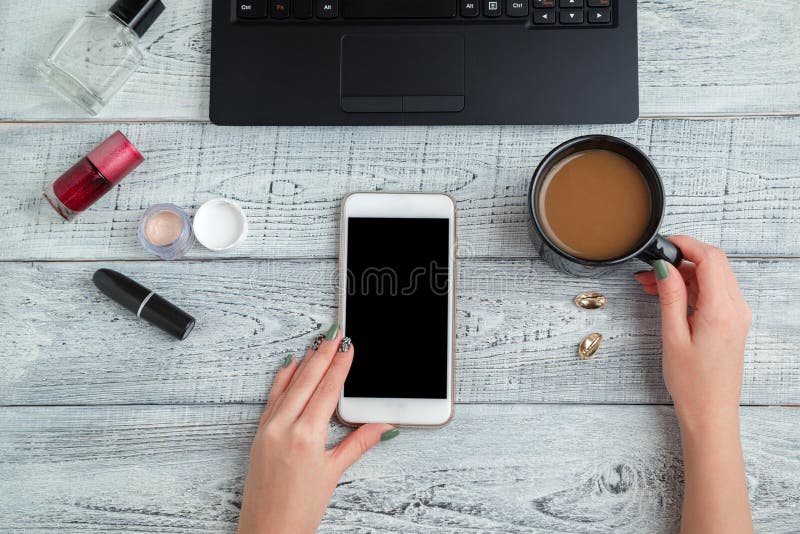 Scrivania posto di lavoro femminile mani, smartphone, laptop, Coppa del caffè, profumi e cosmetici da donna la vista dall'alto st immagini stock Scrivania posto di lavoro femminile mani, smartphone, laptop, Coppa del caffè, profumi e cosmetici da donna la vista dall'alto st immagini stock
