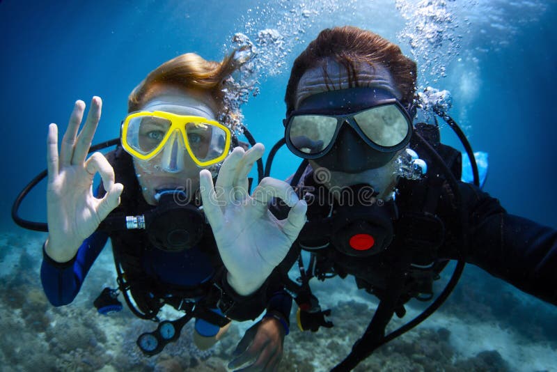 Sott'acqua il germoglio di una giovane coppia diving con immersioni in un mare tropicale e mostrando il segnale di 