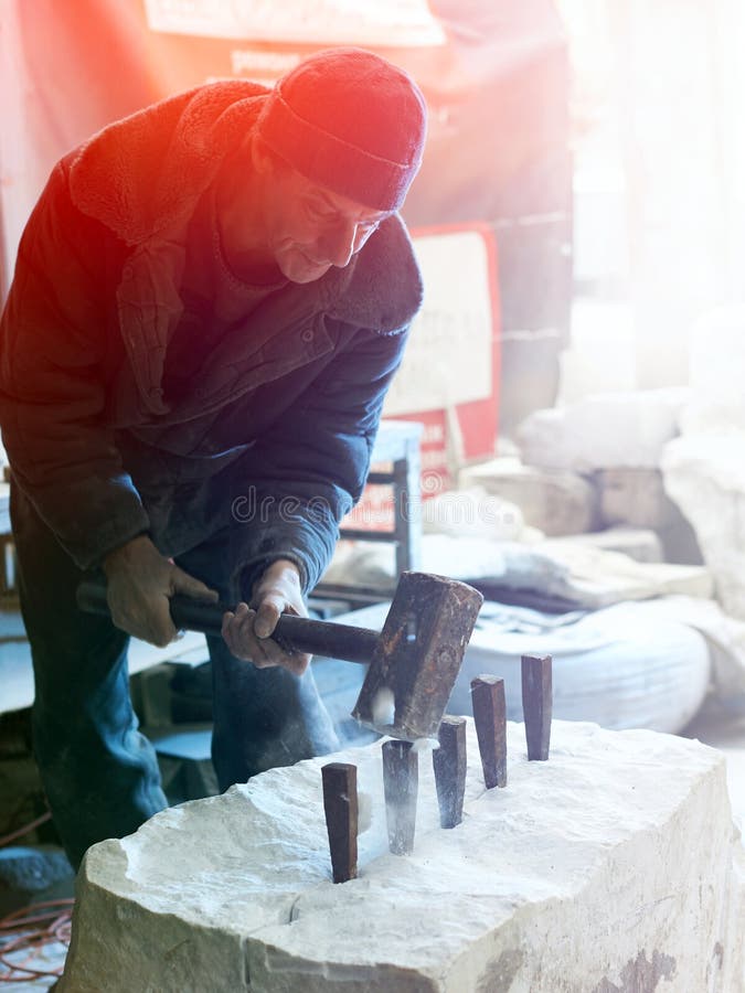 The sculptor of the stone-maker strikes with a heavy hammer on w stock photography The sculptor of the stone-maker strikes with a heavy hammer on w stock photography