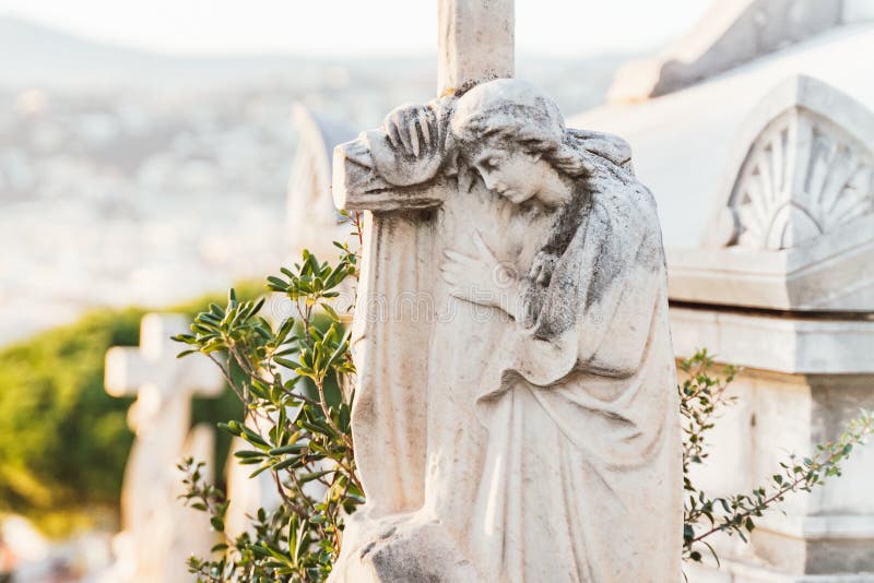 Sculpture of a angel with a cross at old cemetery. Closeup of stoned angel with crying at cemetery. Graveyard old weathered stone