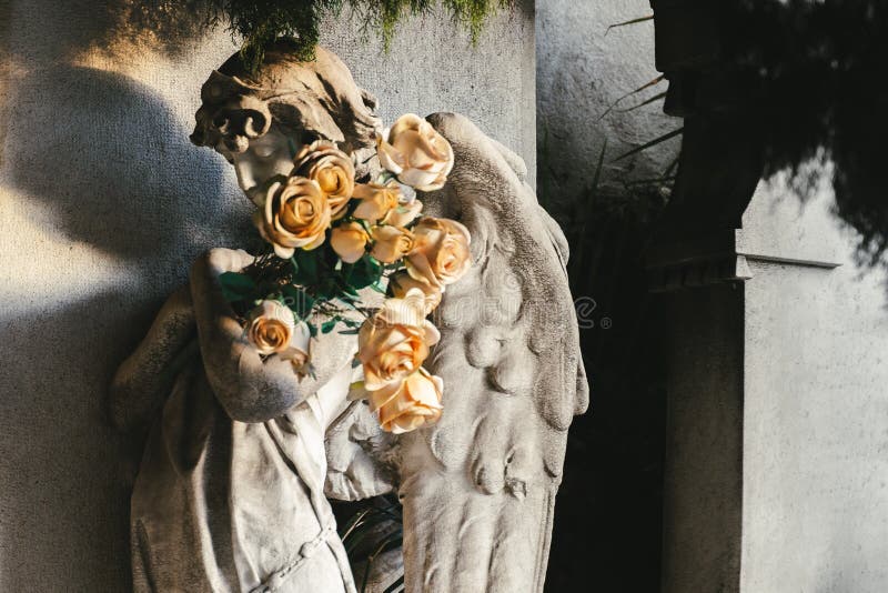 Sculpture of stone granite angel with flowers on headstone in a old cemetery.  black and white stoned angel with yellow roses on funeral. Graveyard ancient praying statue on funeral. Death, loss, condolence concept. Sculpture of stone granite angel with flowers on headstone in a old cemetery.  black and white stoned angel with yellow roses on funeral. Graveyard ancient praying statue on funeral. Death, loss, condolence concept