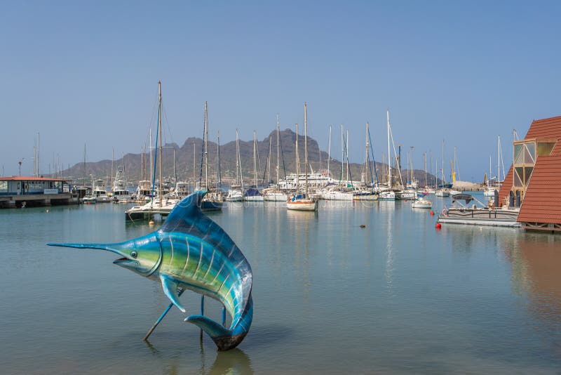 Sculpture of a swordfish at the Port of Mindelo, Sao Vicente island with boats and mountain in background. Sculpture of a swordfish at the Port of Mindelo, Sao Vicente island with boats and mountain in background