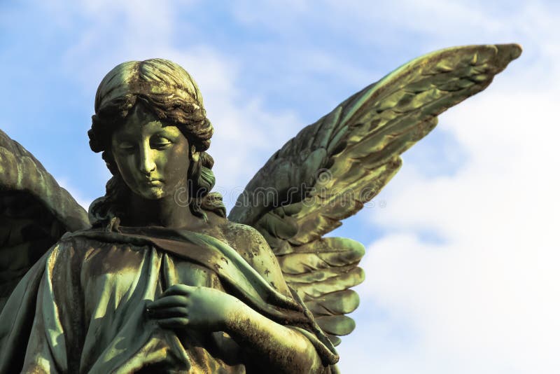 Sculpture en bronze en ange gardien triste avec de longues ailes ouvertes à travers le cadre contre un ciel blanc bleu lumineux images stock Sculpture en bronze en ange gardien triste avec de longues ailes ouvertes à travers le cadre contre un ciel blanc bleu lumineux images stock