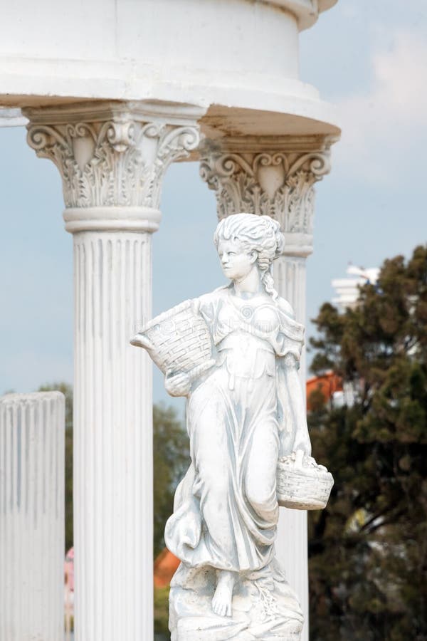 Sculpture of young woman holding basket full of grapes or fruits near corinthian columns in a public park. Replica of royalty free stock photo Sculpture of young woman holding basket full of grapes or fruits near corinthian columns in a public park. Replica of royalty free stock photo