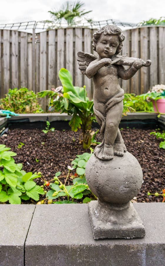 Scultura di pietra di piccolo angelo che tiene una decorazione del giardino dello strumento del violino fotografie stock Scultura di pietra di piccolo angelo che tiene una decorazione del giardino dello strumento del violino fotografie stock