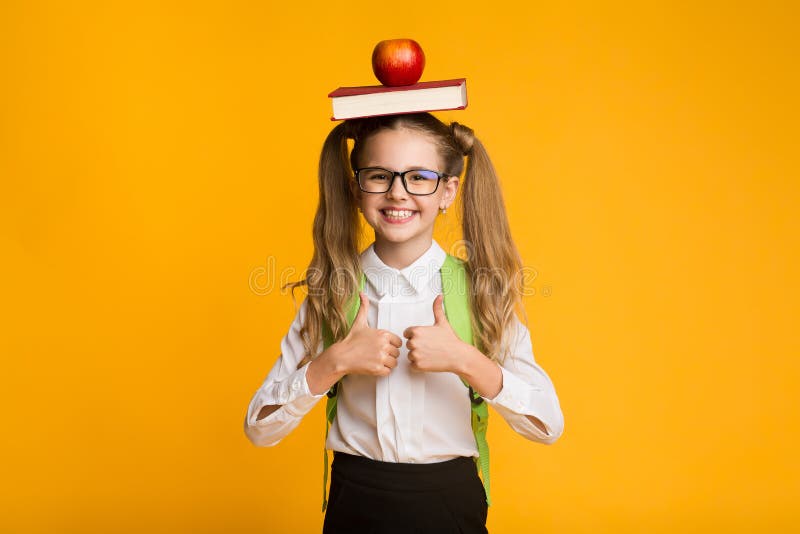 Scuola Che Gestisce Pollice In Mano Per Tenere Libri E Mele Sulla Testa fotografie stock Scuola Che Gestisce Pollice In Mano Per Tenere Libri E Mele Sulla Testa fotografie stock