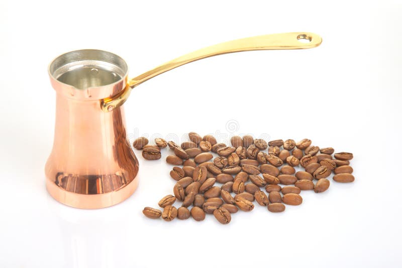 Scutec tradițional din cupru cu mâner auriu lângă o grămadă de boabe de cafea așezate pe o suprafață albă curată, ideală pentru go royalty free stock image