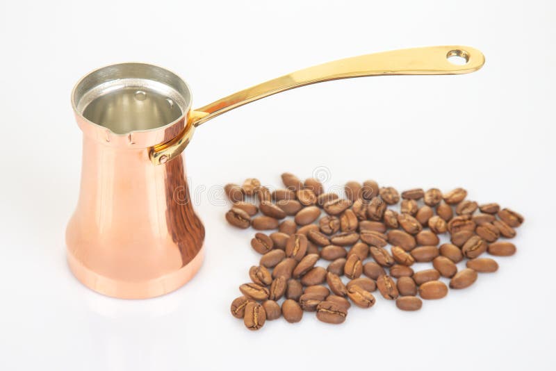 Scutec tradițional din cupru cu mâner auriu lângă o grămadă de boabe de cafea așezate pe o suprafață albă curată, ideală pentru go stock photography