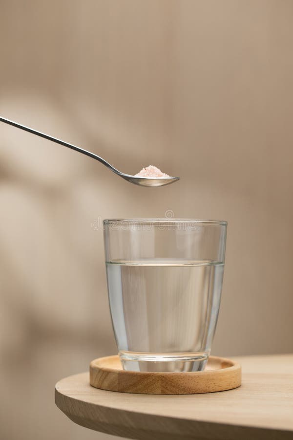 Se está agregando una cuchara de sal himalaya a un vaso de agua potable fotos de archivo