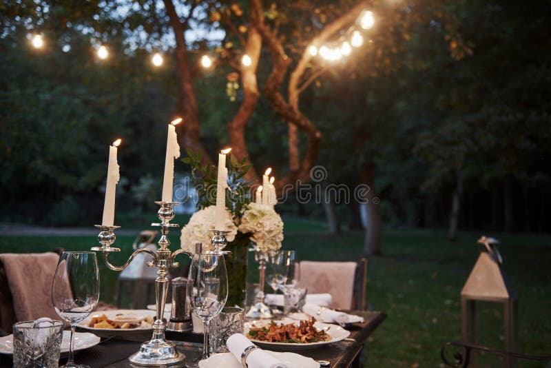 Se puede ver poco viento a través del fuego de las velas Mesa preparada para la comida y los visitantes Hora de la noche foto de archivo libre de regalías Se puede ver poco viento a través del fuego de las velas Mesa preparada para la comida y los visitantes Hora de la noche foto de archivo libre de regalías