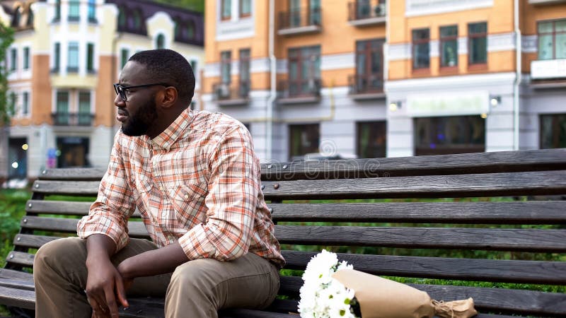 Sad african man sitting lonely on city bench with flower bouquet, failed date, stock photo. Sad african man sitting lonely on city bench with flower bouquet, failed date, stock photo