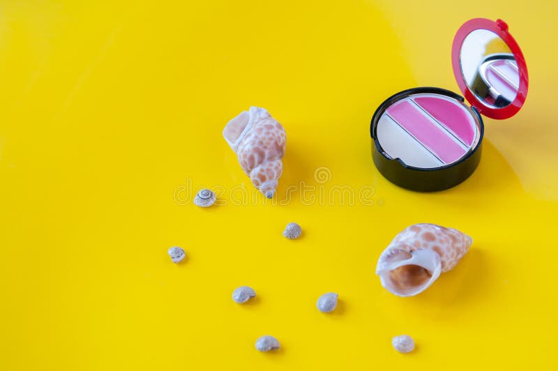 Sea shells and lip gloss on a yellow background