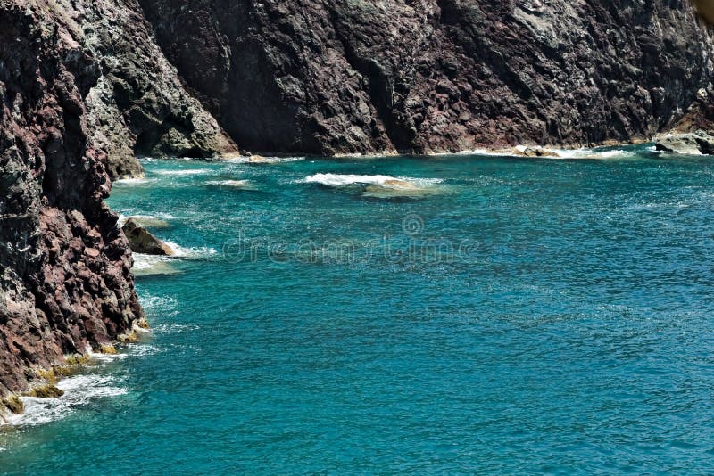 Sea waves break on the rocks of the Ligurian mountain. Near the Cinque Terre a seascape with blue sea and dark red rocks. Village stock photography Sea waves break on the rocks of the Ligurian mountain. Near the Cinque Terre a seascape with blue sea and dark red rocks. Village stock photography