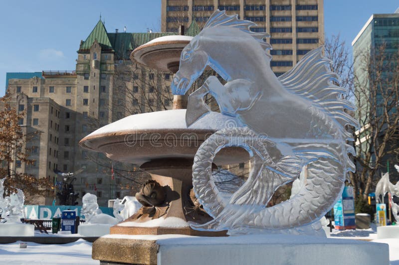 Ice sculpture in Ottawa, on a sunny day with city buildings behind. Ice scupltrure is of a seahorse creature, with horse head and fish or mermaid tail. Ice sculpture in Ottawa, on a sunny day with city buildings behind. Ice scupltrure is of a seahorse creature, with horse head and fish or mermaid tail.