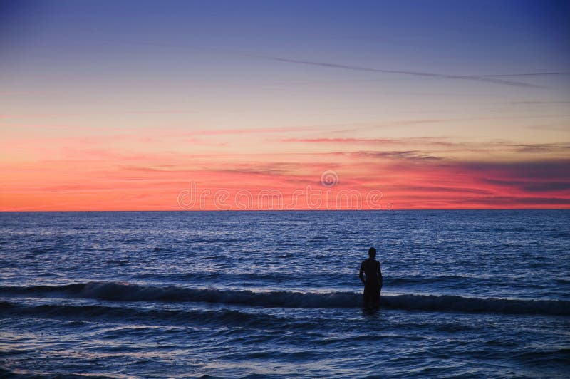 Person standing in shallow water looking at the seascape at dusk. Serene beach atmosphere stock images, royalty-free photos and pictures