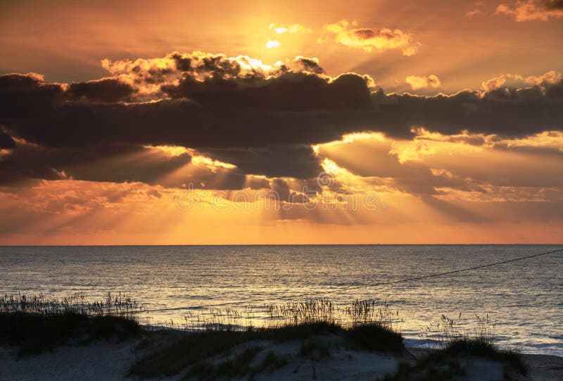 East coast landscape of sun rising over the Altantic Ocean in Frisco North Carolina shining rays through the openings in the cloud formations in the sky. East coast landscape of sun rising over the Altantic Ocean in Frisco North Carolina shining rays through the openings in the cloud formations in the sky.