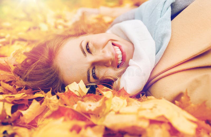 Beautiful happy woman lying on autumn leaves