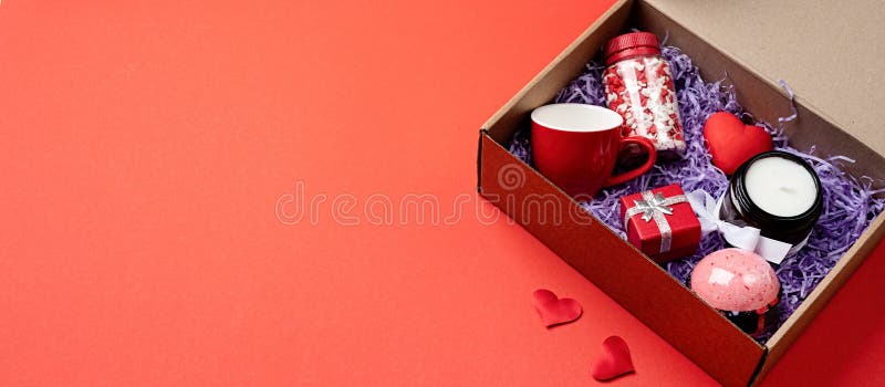 Seasonal gift box for valentine day with candle, red cup and heart shape sweets on red background, banner