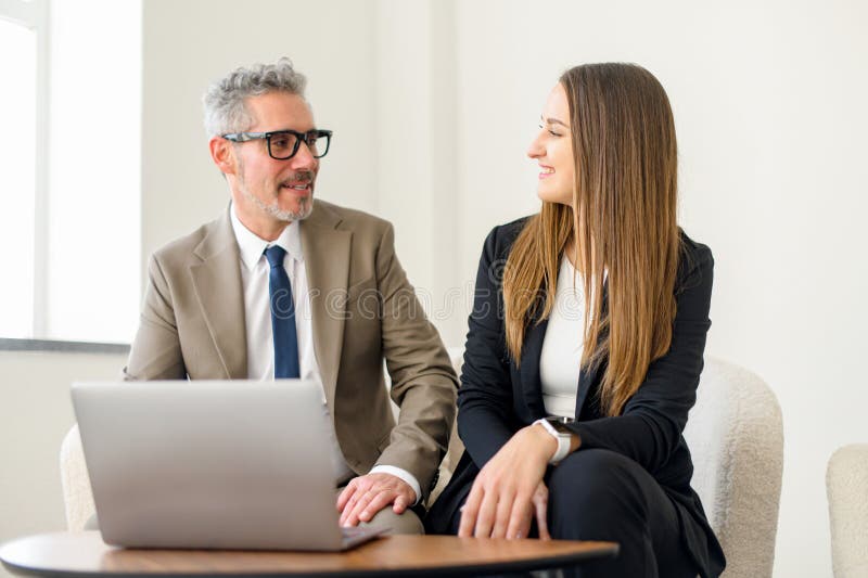 Seasoned businessman with grey hair and a younger female colleague are both engaged with a laptop royalty free stock photo