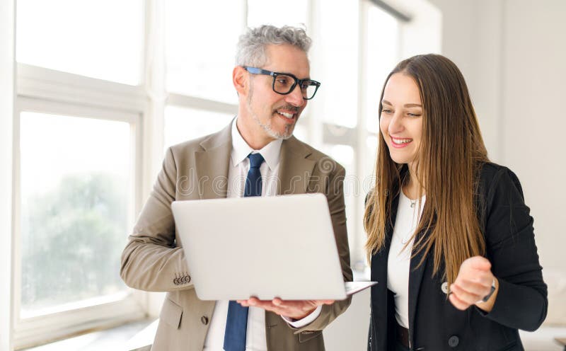 Seasoned businessman with grey hair and a younger female colleague are both engaged with a laptop stock photo