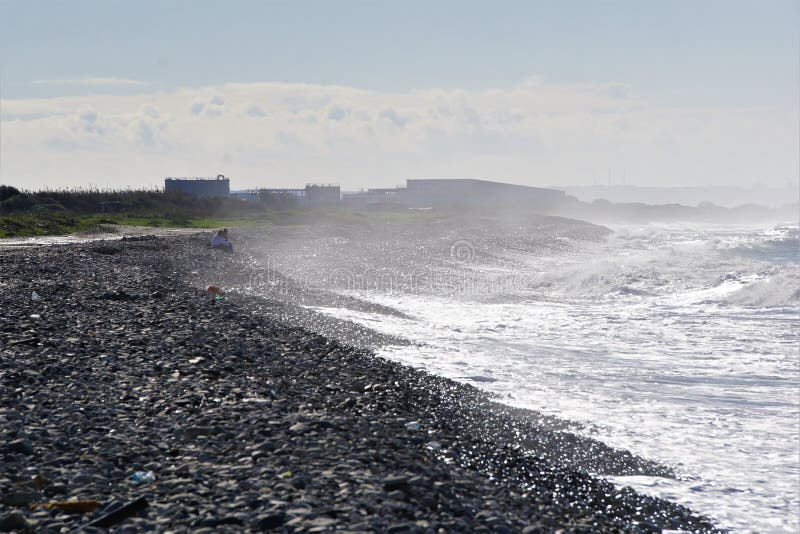 Seaspray fogs stony beach as friends look out to sea