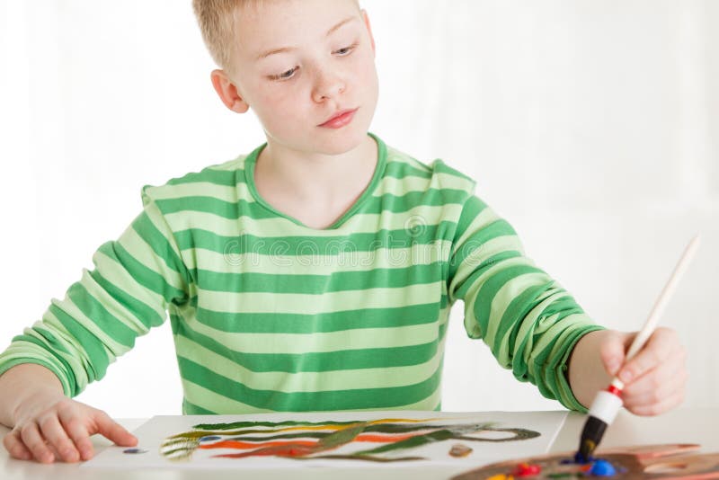 Seated boy paints with brush on white paper stock images Seated boy paints with brush on white paper stock images