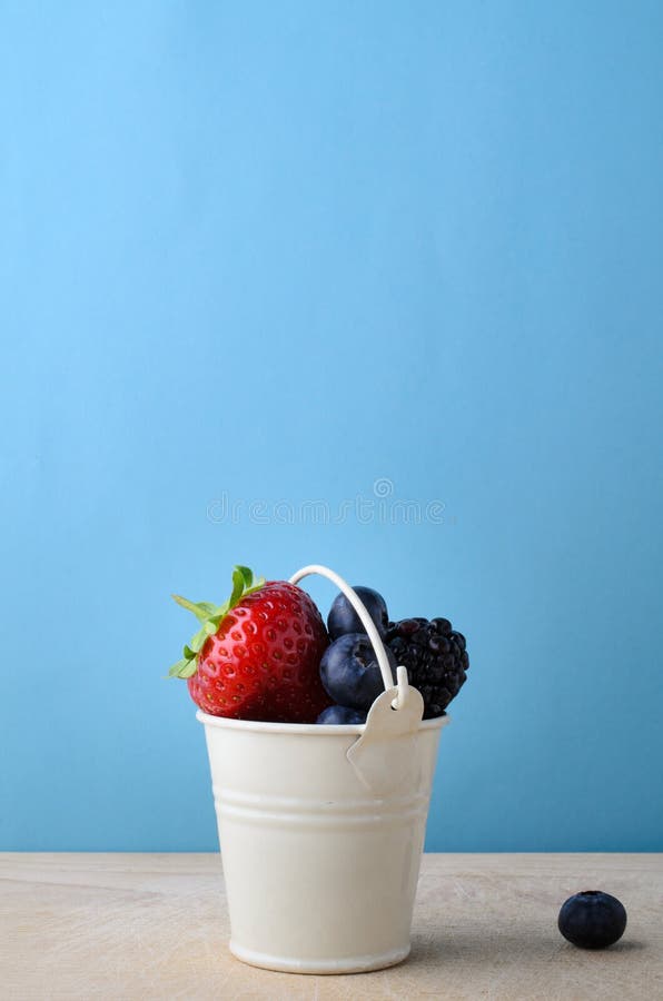 Seau d'émail rempli de baies de fruit frais sur le bois avec le bleu photos stock Seau d'émail rempli de baies de fruit frais sur le bois avec le bleu photos stock