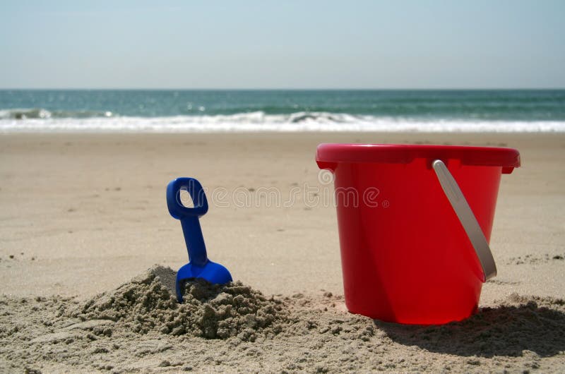 Red pail and blue shovel in the sand at the beach. Red pail and blue shovel in the sand at the beach.