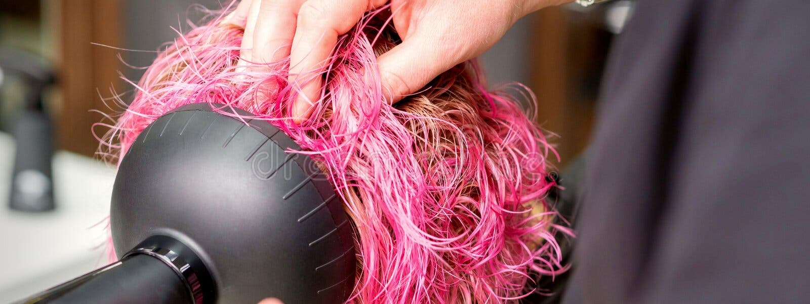 Secador de cabelo preto na mão de uma mulher em um fundo rosa