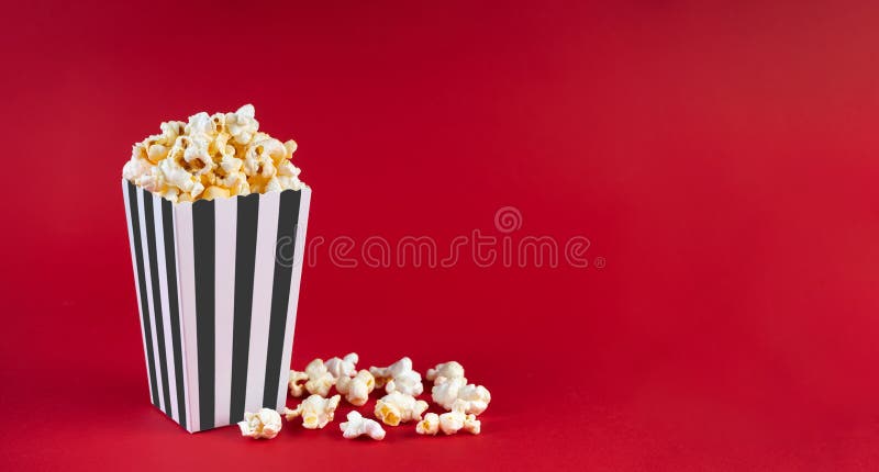 Secchio di cartone bianco a strisce nero con popcorn al formaggio saporito isolato sullo sfondo rosso immagine stock