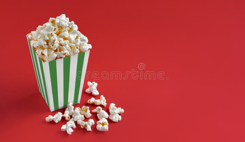 Secchio di cartone a strisce bianche verde con popcorn al formaggio saporito isolato sullo sfondo rosso immagini stock