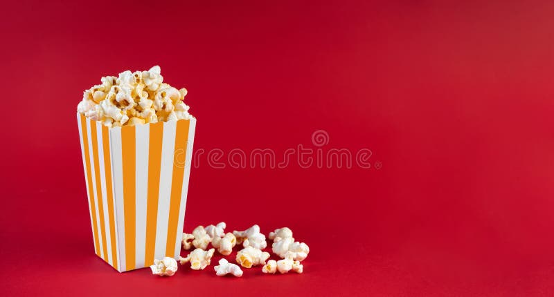 Secchio di cartone a strisce gialle con formaggio di popcorn di cattivo gusto isolato su fondo rosso immagini stock