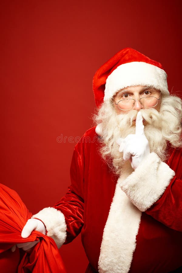 Santa Claus with sack of Christmas presents keeping forefinger by mouth. Santa Claus with sack of Christmas presents keeping forefinger by mouth