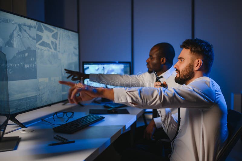 In the Security Control Room Two Officers Monitoring Multiple Screens for Suspicious Activities royalty free stock photo