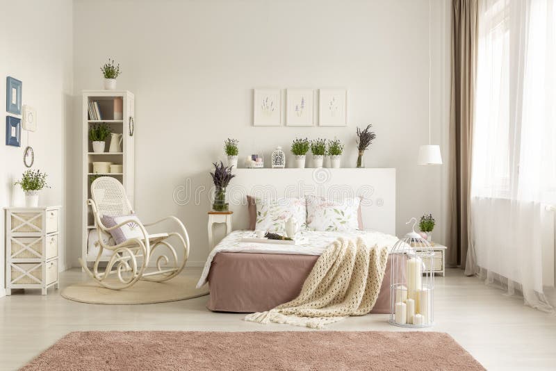 Sedia di oscillazione accanto al letto con la coperta nell'interno bianco spazioso della camera da letto con tappeto rosa Foto re