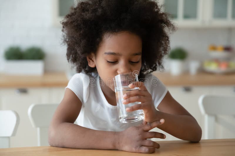 Sedienta pequeña niña afroamericana rizada niña pequeña beberna agua. foto de archivo libre de regalías
