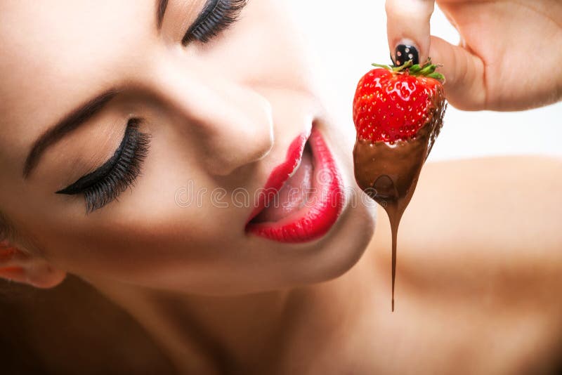 Seducción - labios femeninos rojos que comen las fresas del chocolate imágenes de archivo libres de regalías Seducción - labios femeninos rojos que comen las fresas del chocolate imágenes de archivo libres de regalías