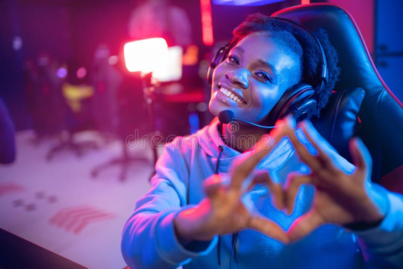 Seducente ragazza africana mostra l'insegna del cuore con un giocatore professionista che gioca online videogame a colori fotografia stock libera da diritti