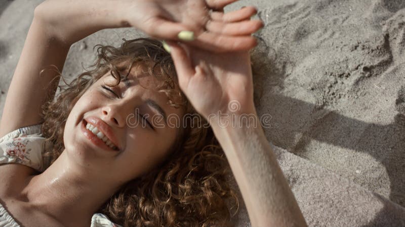 Seductive lady lying beach sand hiding face behind hands closeup. Woman smiling