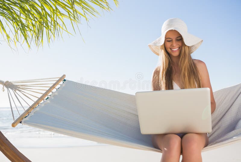 Seduta bionda felice sull'amaca facendo uso del computer portatile immagine stock libera da diritti Seduta bionda felice sull'amaca facendo uso del computer portatile immagine stock libera da diritti