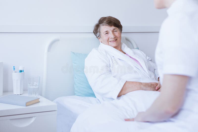 Seduta senior sorridente nel letto di ospedale dopo chirurgia fotografie stock Seduta senior sorridente nel letto di ospedale dopo chirurgia fotografie stock