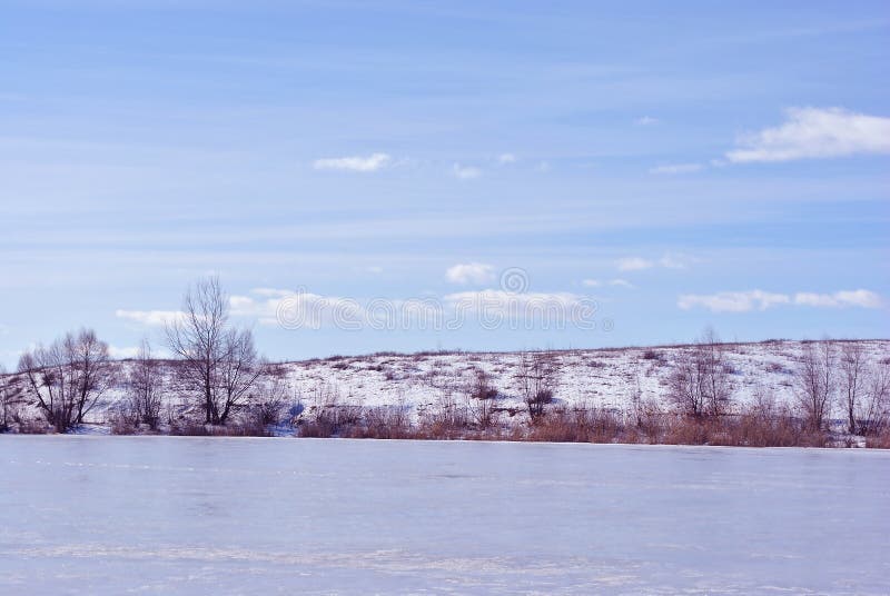 Seebank bedeckt mit Eis, Bäume ohne Blätter auf Hügel, Hintergrund des bewölkten Himmels stockbild Seebank bedeckt mit Eis, Bäume ohne Blätter auf Hügel, Hintergrund des bewölkten Himmels stockbild