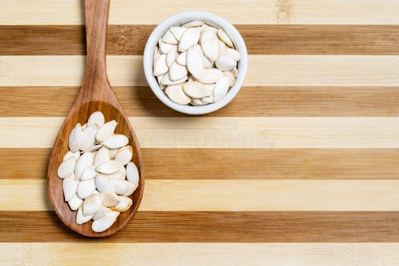 Seed of pumpkin in wooden spoon and pot on bamboo striped table