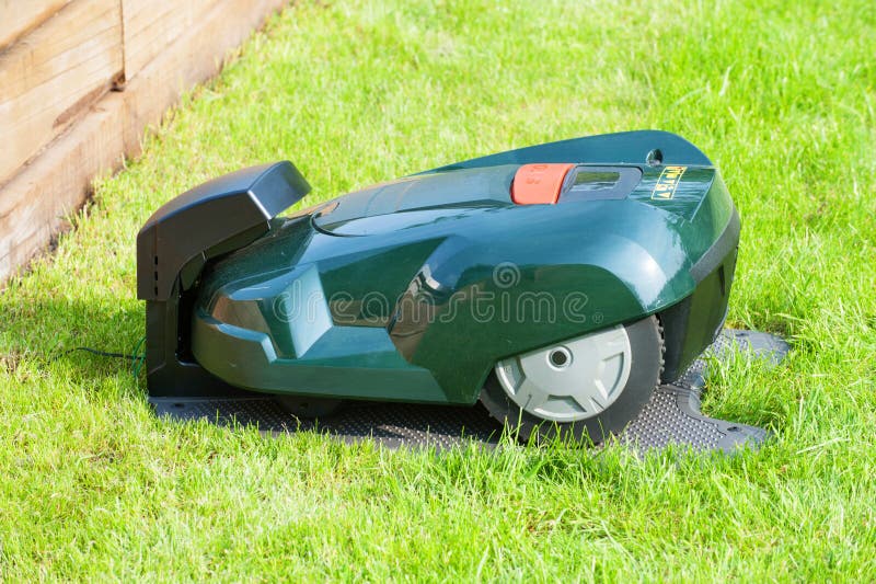 A modern automatic lawn mower in docking station for charging battery. Its a self mowing device. Image taken outside in garden. A modern automatic lawn mower in docking station for charging battery. Its a self mowing device. Image taken outside in garden.