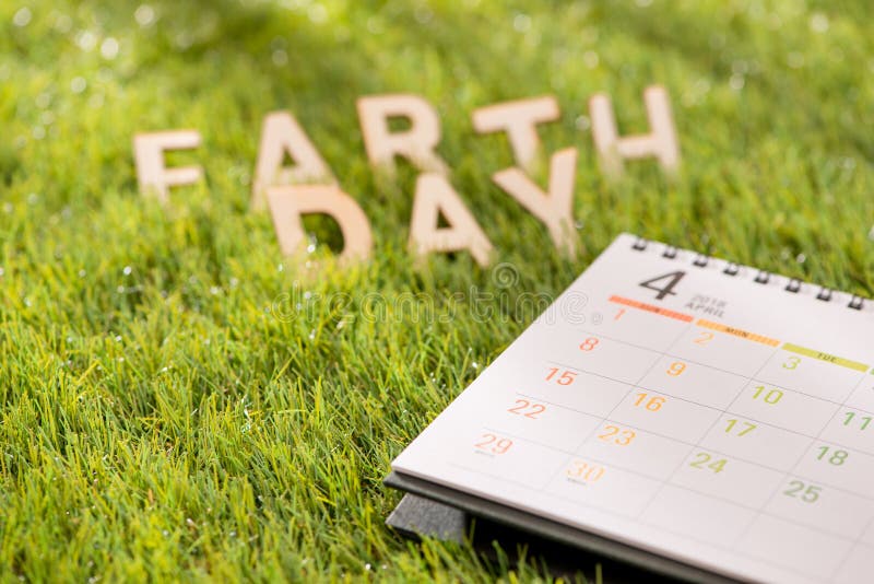 Segni il concetto con lettere felice del giorno di terra con il calendario su erba verde immagine stock Segni il concetto con lettere felice del giorno di terra con il calendario su erba verde immagine stock