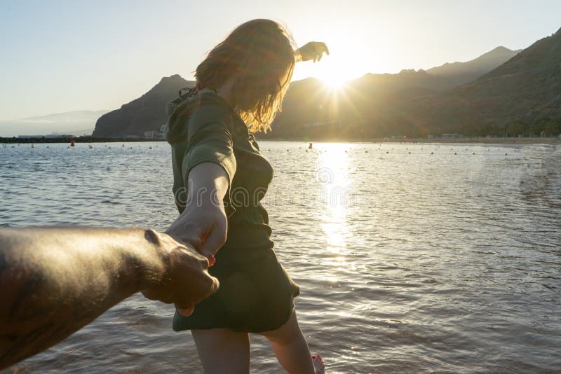 Seguito della fidanzata con un vestito estivo che corre e tiene la mano del fidanzato sulla spiaggia al tramonto Felice coppia in fotografie stock